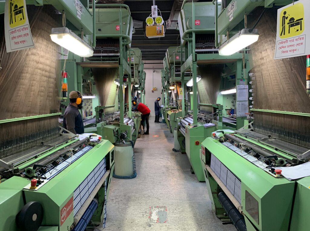 Industrial production line in Narayanganj, Bangladesh with workers at textile machines.